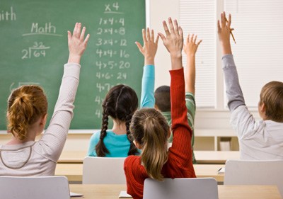 Children raising their hand in a school building's classroom.